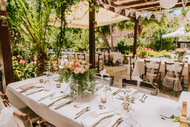Long reception table with pink and peach flowers under a shaded pergola