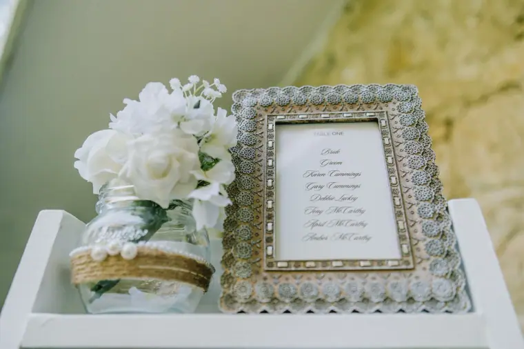 Framed menu beside a jar of white hydrangeas on a white shelf