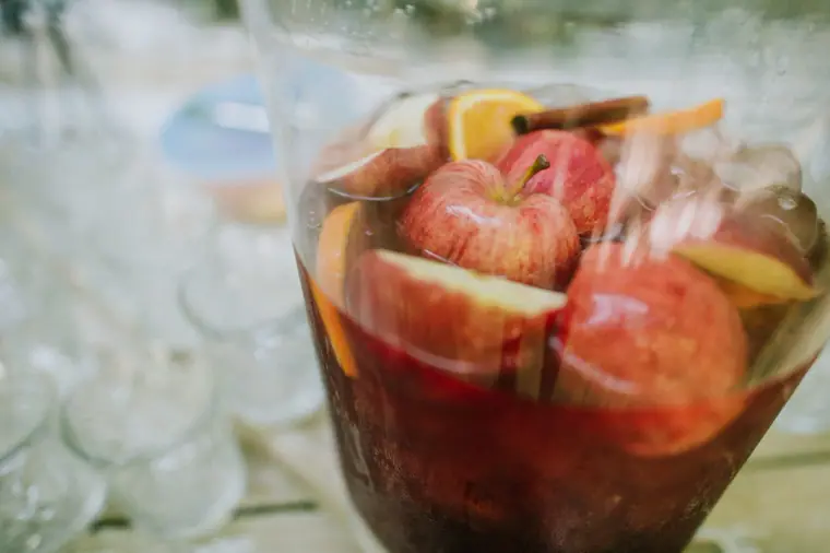 Jug of sangria with apple and orange slices on the drinks table