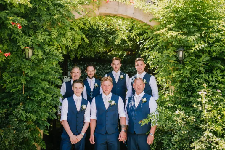 Sean and his groomsmen in navy waistcoats under the ivy-covered stone arch