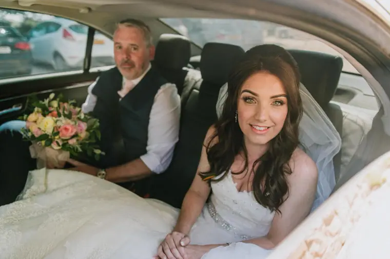 Claire smiling with her father in the back of the wedding car
