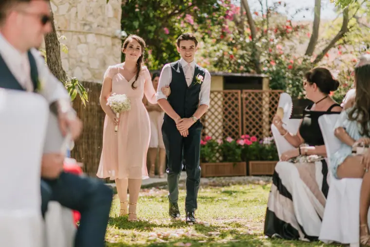 Bridesmaid in blush pink walking down the grassy aisle as guests watch
