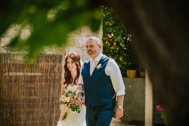 Claire walking down the aisle on her father's arm, framed by leaves
