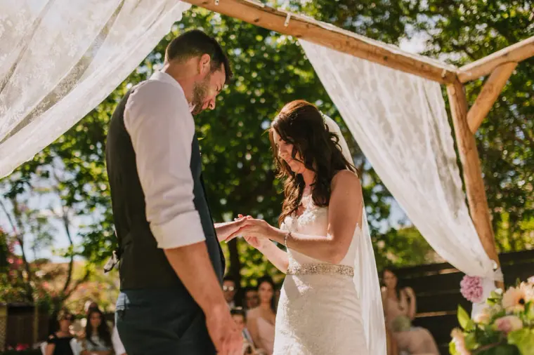 Claire and Sean exchanging rings under the lace-draped wooden arch