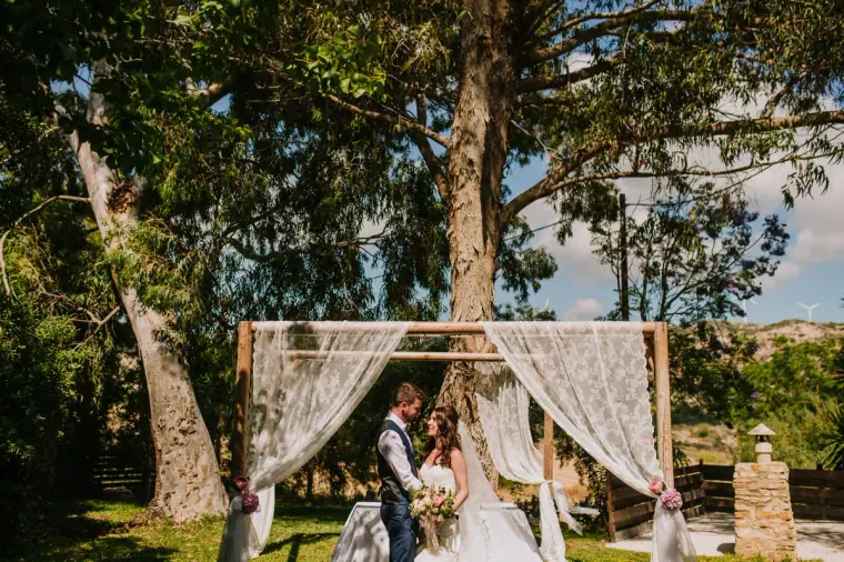 Wide view of the outdoor ceremony arch under tall trees at Vasilias Nikoklis Inn, Paphos