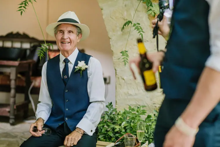 Smiling guest in a panama hat and navy waistcoat sitting in the courtyard