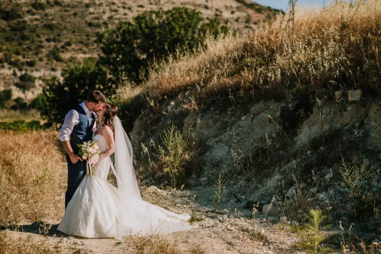 Claire and Sean kissing on a dusty hillside track among dry grasses