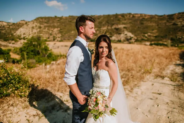 Sean and Claire standing in a golden field with hills behind, near Vasilias Nikoklis Inn