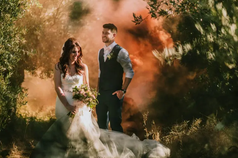 Claire and Sean posing in the olive grove as orange smoke drifts around them