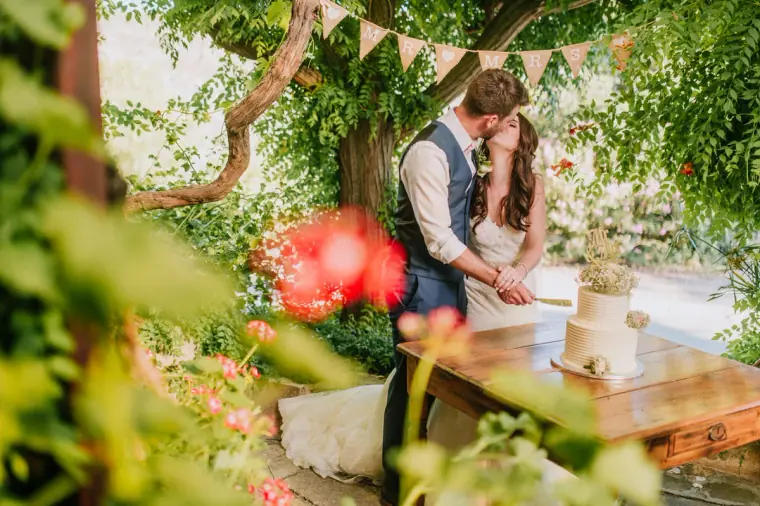 Claire and Sean kissing as they cut the cake beneath the trees