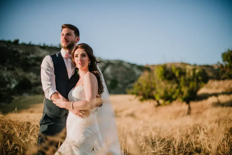Sean holding Claire from behind in a golden field with hills behind