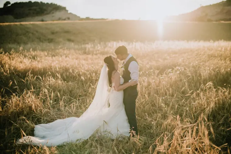 Claire and Sean kissing in tall grass as the sun sets over the hills