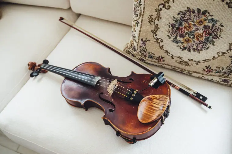 Violin and bow resting on a white sofa beside an embroidered cushion