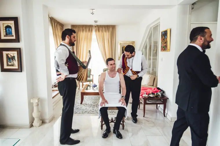 Angelos seated in a vest as musicians and family gather for the Cypriot groom's dressing