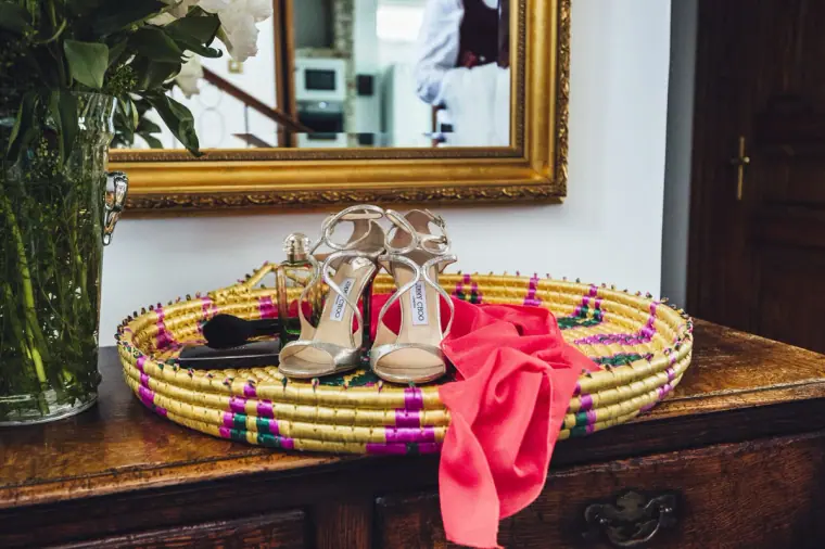 Bridal shoes and a pink ribbon in a colourful woven basket on a dresser