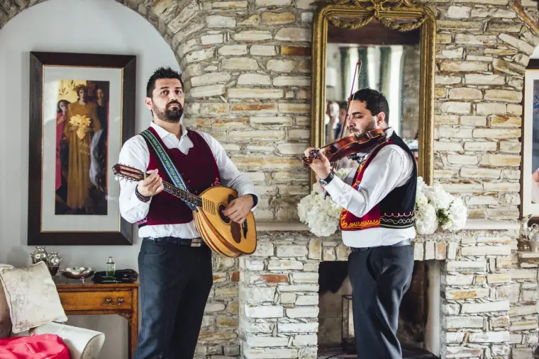 Traditional musicians with lute and violin playing beside a stone fireplace