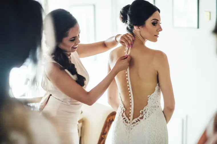Bridesmaid fastening the buttons on the back of Ruby's lace gown