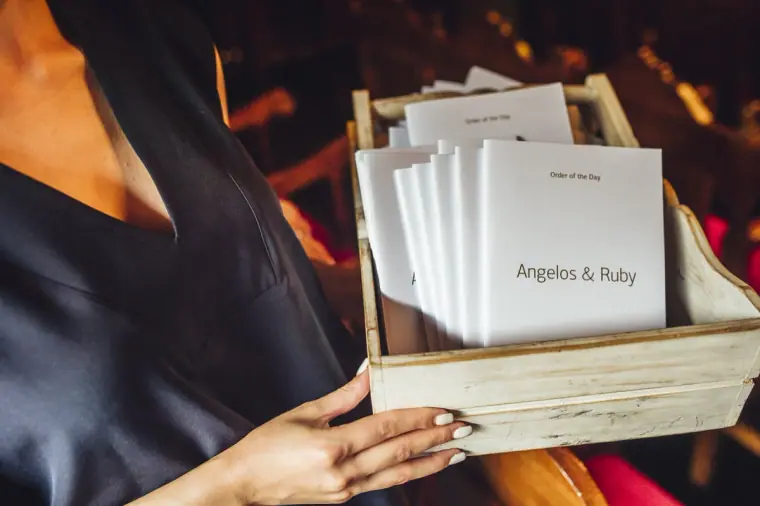 Box of Angelos and Ruby order-of-service booklets held by a guest