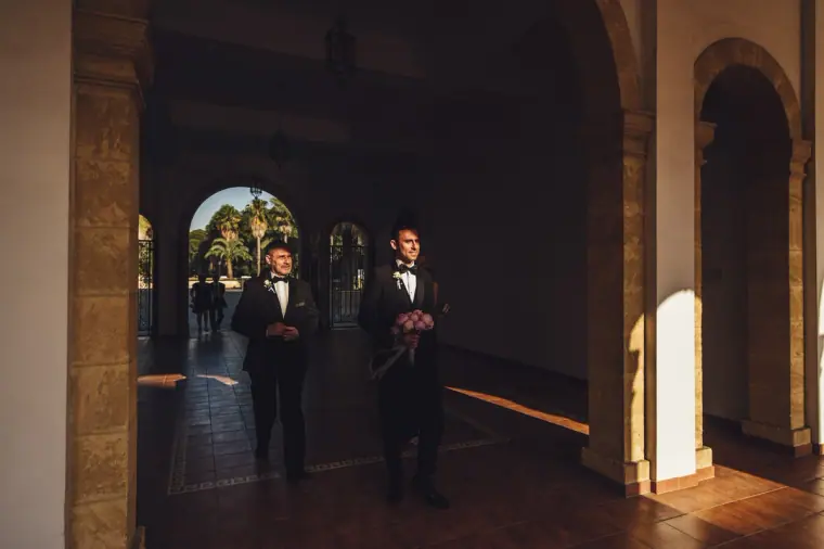 Groom and best man waiting in a shaded stone arcade
