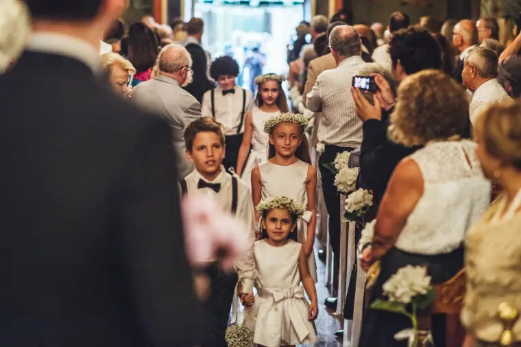 Flower girls and page boy walking down the crowded church aisle