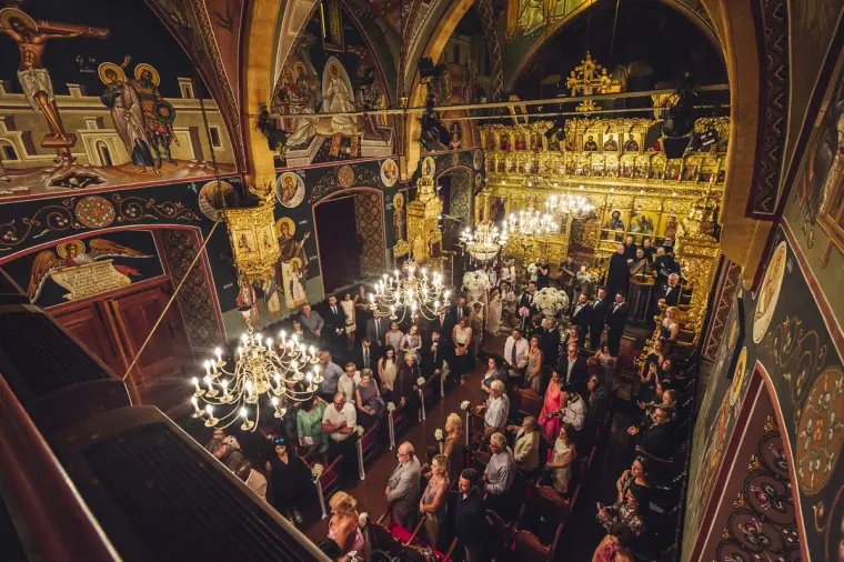 Packed Orthodox church with frescoed walls and chandeliers, seen from above