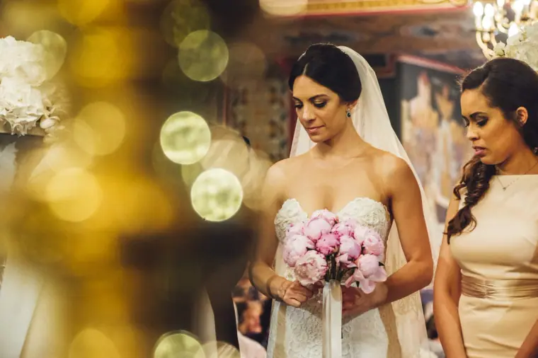 Ruby holding her pink peony bouquet beside a bridesmaid in the church