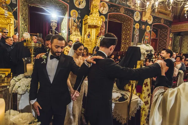 Groom and best men in tuxedos during the Orthodox crowning ceremony in a gilded Nicosia church