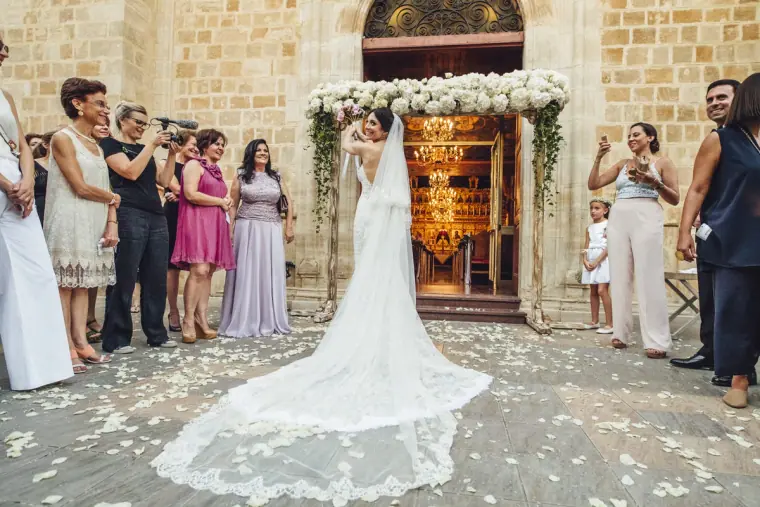Bride's long lace train spread across the petal-strewn church steps as guests watch