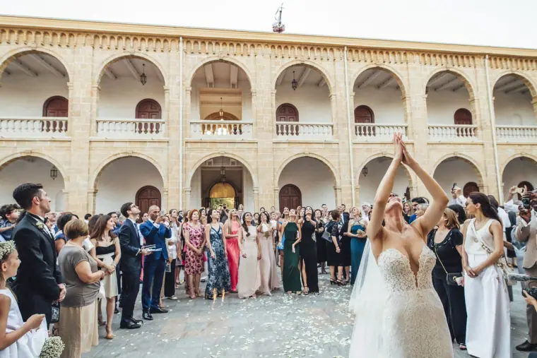 Bride throwing her bouquet in the arcaded courtyard ringed by guests