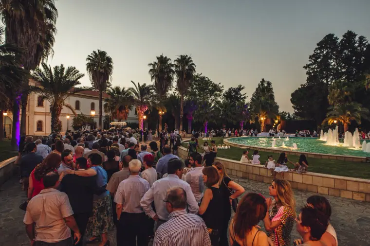 Crowd of guests gathered by a fountain among palm trees at twilight