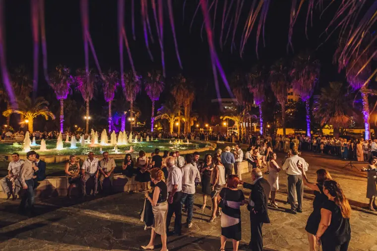 Guests dancing beside illuminated fountains under purple-lit palms at night