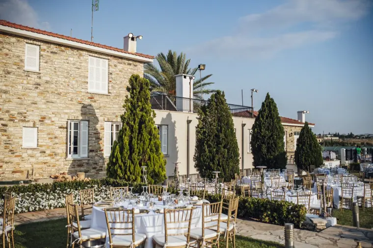 Round tables dressed in white beside a stone villa and cypress trees, Nicosia reception