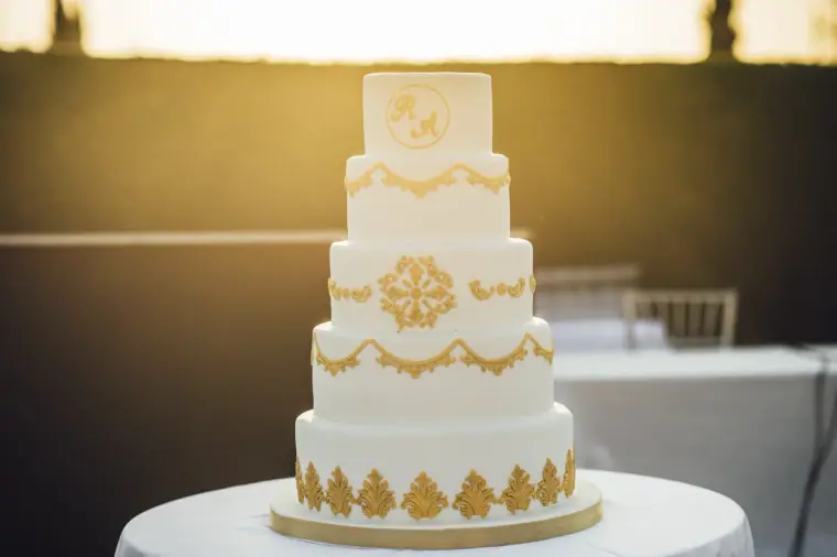 Four-tier white wedding cake with gold baroque detailing at golden hour