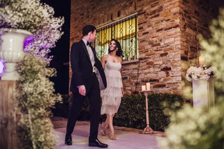 Bride and groom making their entrance past gypsophila and a stone wall in the evening