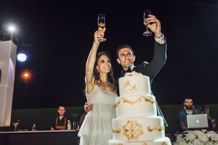 Ruby and Angelos raising champagne glasses behind their gold-detailed cake