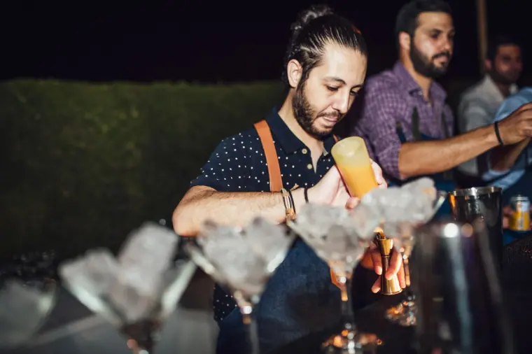 Bartender pouring cocktails into rows of coupe glasses at the reception bar