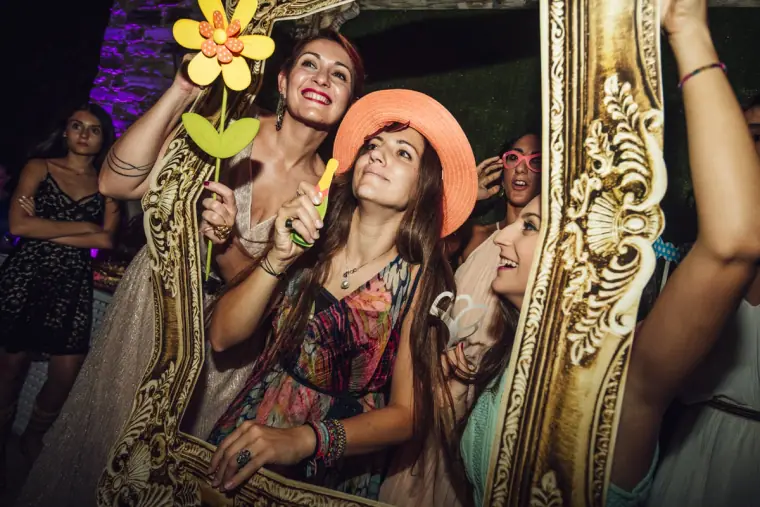 Laughing guests holding up a gilded frame and flower props in the photo booth