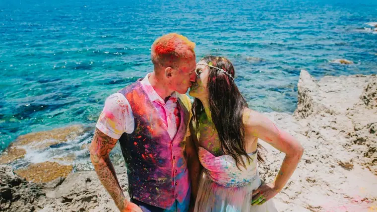 Bride and groom splashed with Holi colours sharing a kiss above the clear sea, Nissi Beach, Ayia Napa