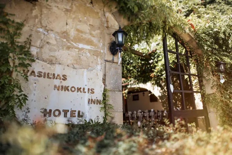 Vasilias Nikoklis Inn hotel sign painted on a stone wall beside a vine-covered gateway