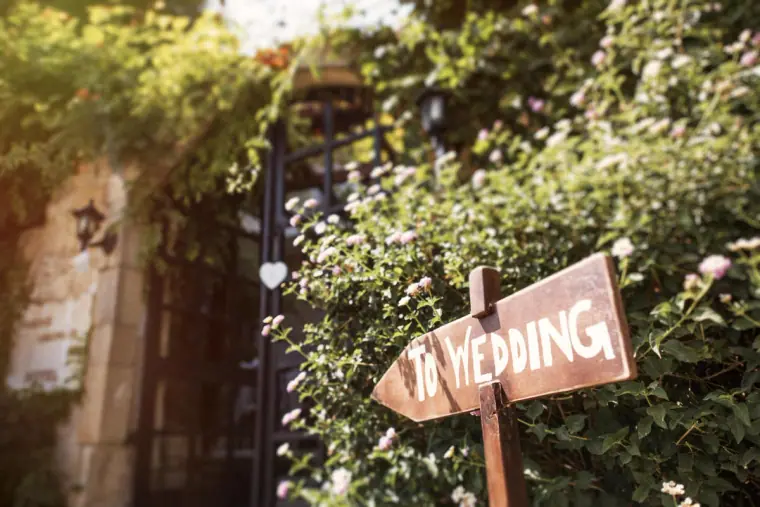 Wooden "The Wedding" direction sign by a vine-draped iron gate at Vasilias Nikoklis Inn