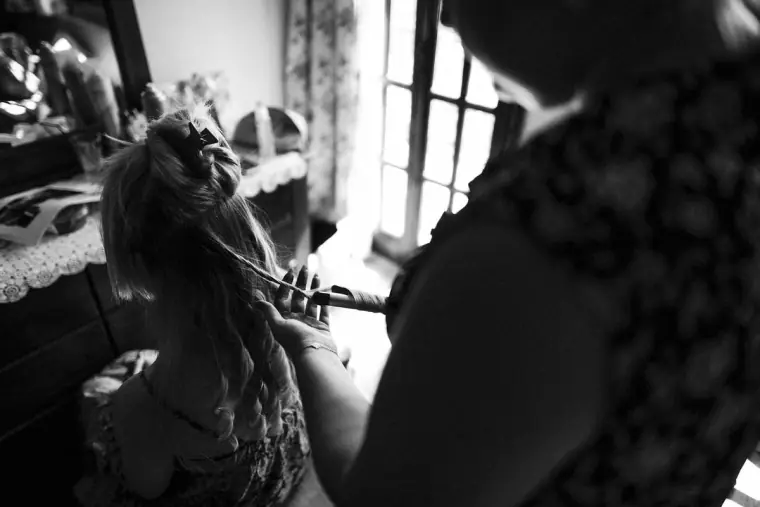 Black-and-white photo of the bride's hair being curled during preparations