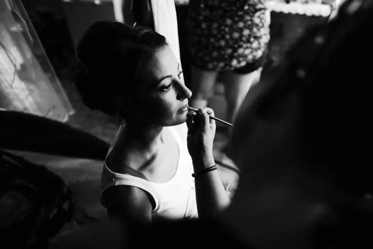 Black-and-white photo of the bride applying lip colour while getting ready