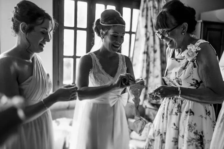 Black-and-white photo of the bride laughing with bridesmaids as they fasten her bracelet