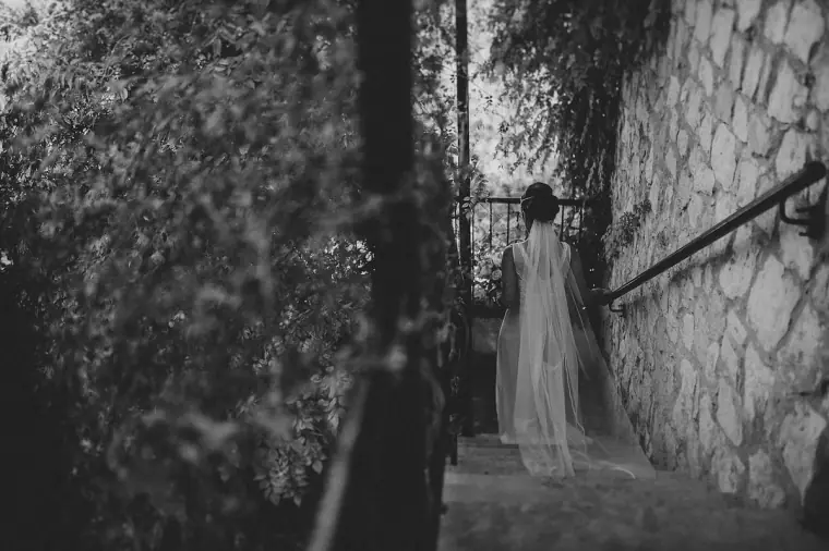 Black-and-white photo of the bride walking down stone steps beneath a long veil