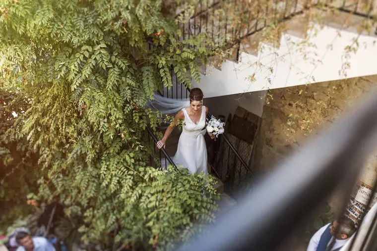 Bride descending a leafy stairway with her bouquet at Vasilias Nikoklis Inn