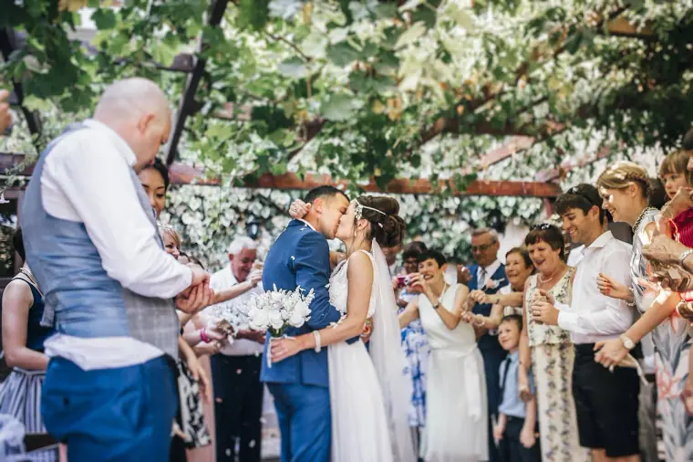 Newlyweds kissing under the vine-covered pergola as guests applaud