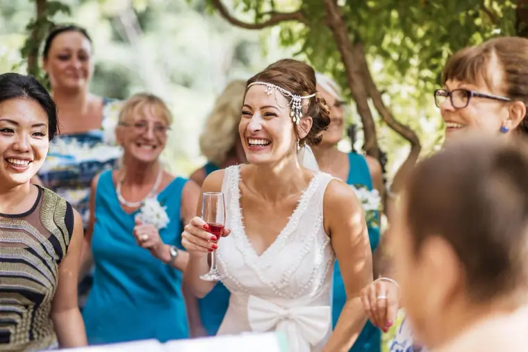 Laughing bride with a glass of rosé among female guests in the courtyard