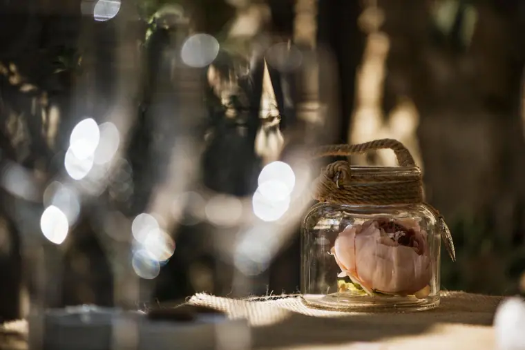 Jar holding a pink rose on the table, surrounded by sparkling glassware