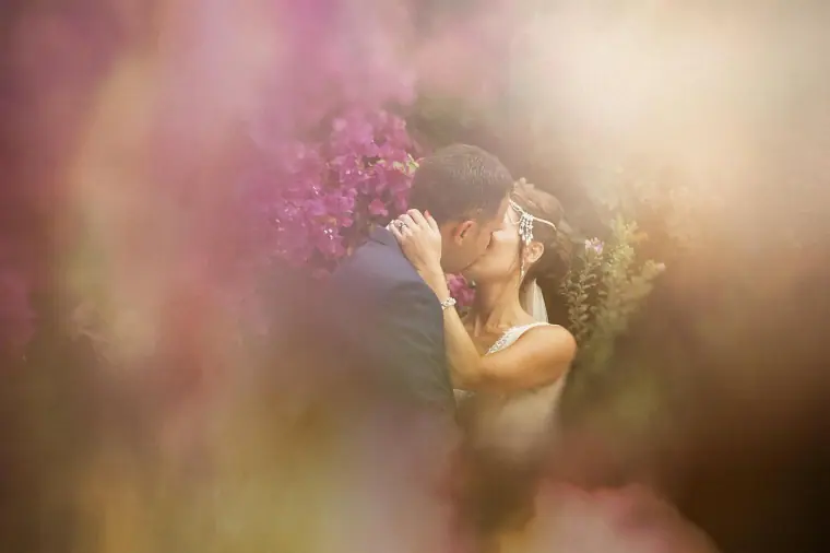 Bride and groom kissing behind a blur of pink bougainvillea