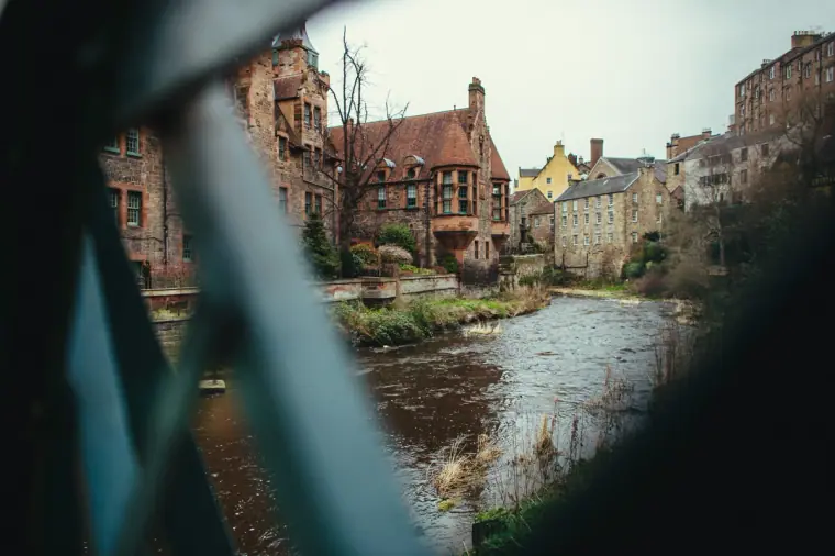 Riverside sandstone buildings in Edinburgh glimpsed through a teal bridge railing